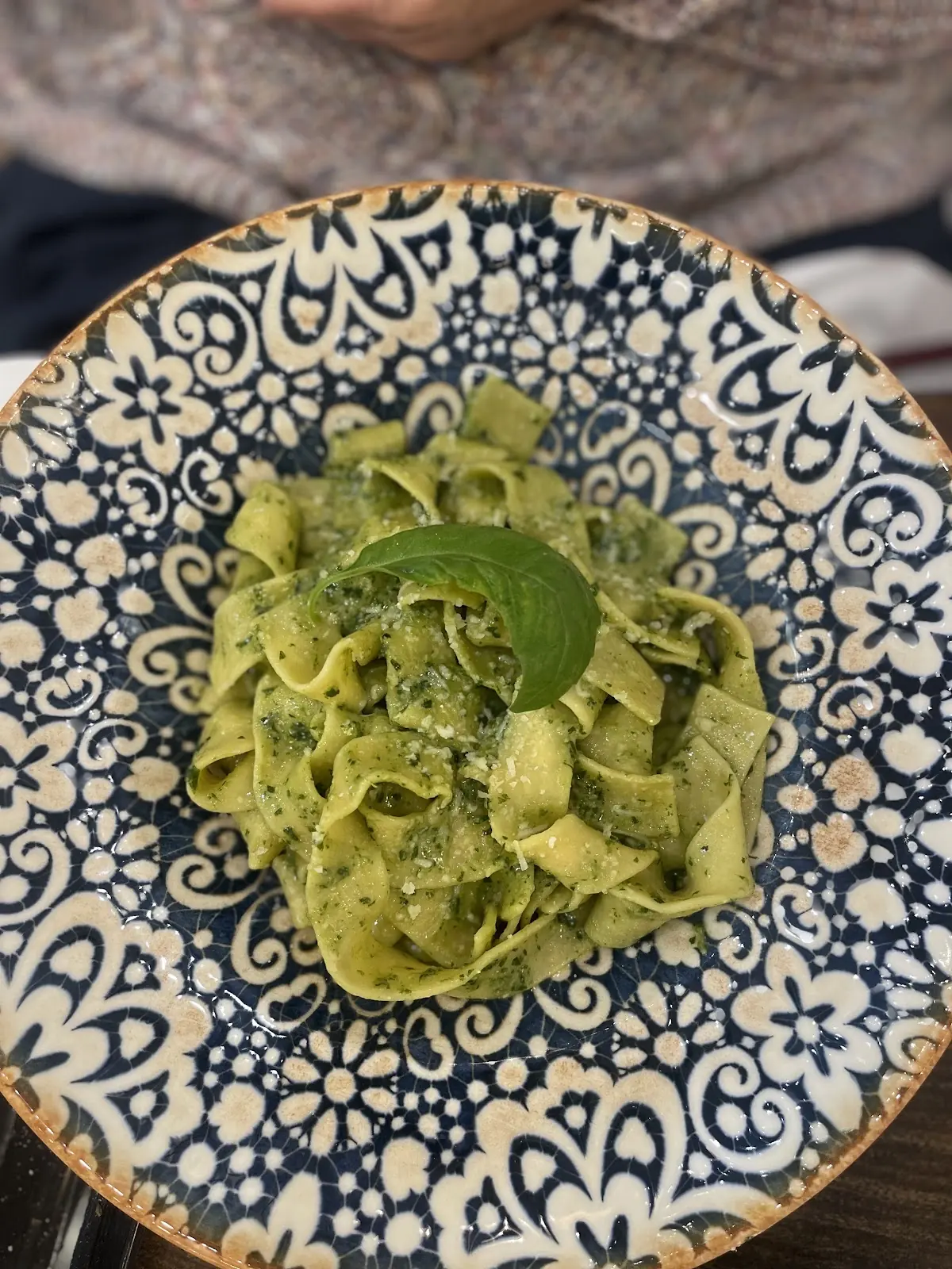 Green pesto tagliatelle topped with fresh basil leaves on a blue-and-white patterned plate
